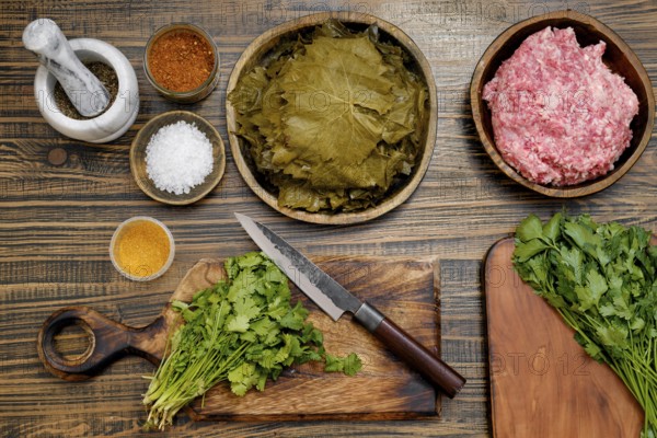 Preparing dolma by assembling marinated grape leaves, ground meat, and herbs on a wooden countertop
