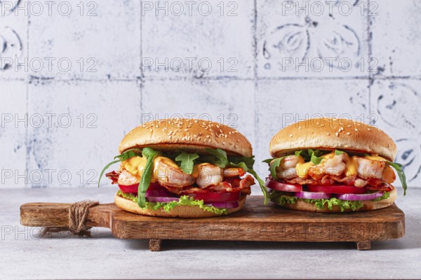 Two shrimp burgers and buns with sesame seeds, bacon, lettuce, tomatoes and onions, On a wooden