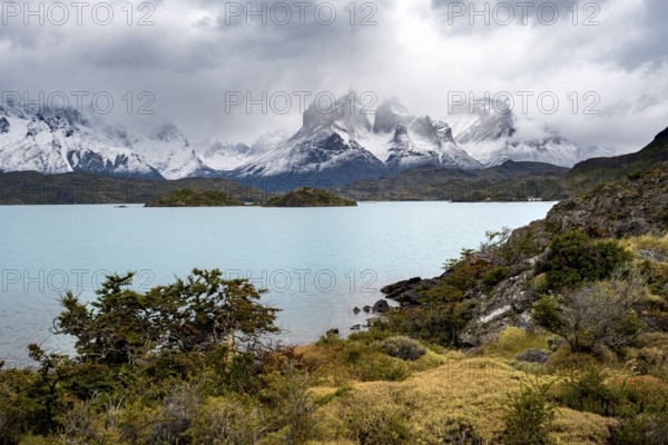 Cloudy mountain range Cuernos del Paine, shore of the blue lake Lago Pehoe in the evening light,