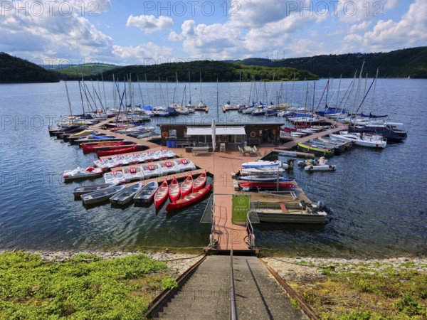 A colourful little marina with boats, sailing boats and pedal boats docked at a jetty on a lake,