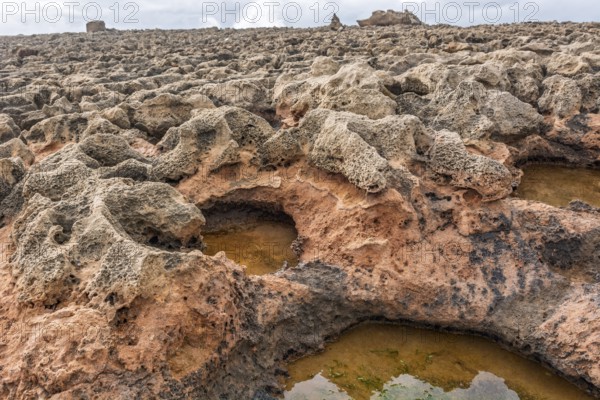 A rocky area with a hole in the ground. The hole is filled with water. The water is brown in colour