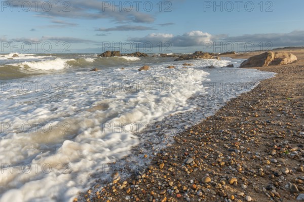 The waves crash gently against a rocky shoreline at sunset, creating a tranquil atmosphere. The
