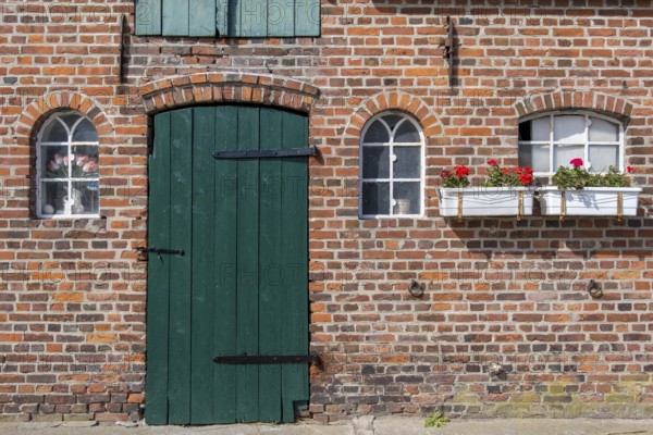 Nostalgic brick wall with green door and white windows, decorated with flower pots, Föhr,