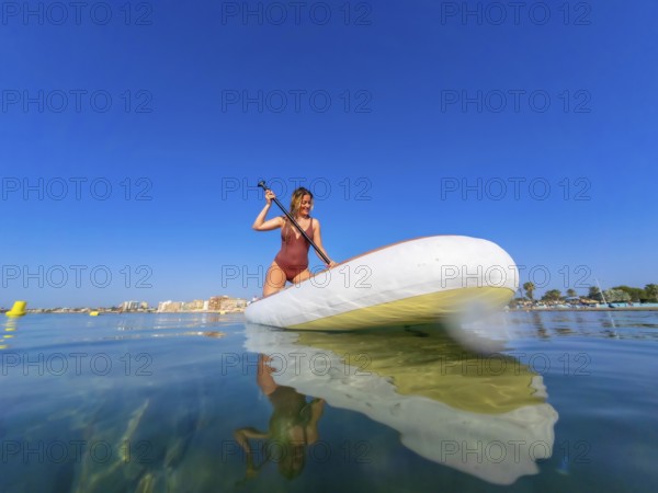 Young woman paddling on a stand up paddle board in the serene sea, soaking up the sun on a