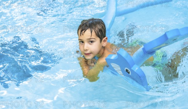 Happy boy enjoying playtime with an inflatable toy whale in a sparkling swimming pool, soaking up