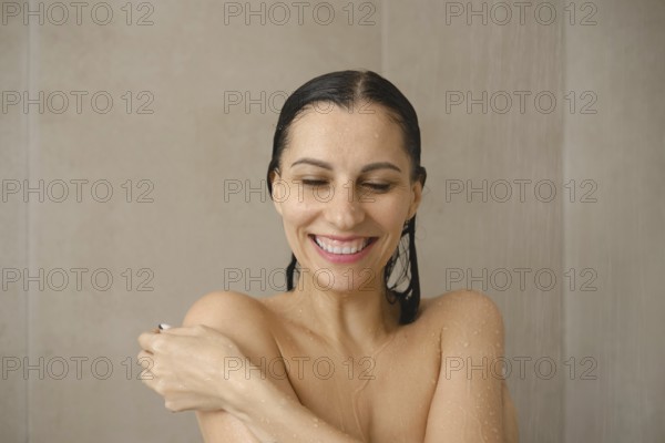 A woman stands under a gentle stream of water in a stylish bathroom, smiling and looking relaxed.