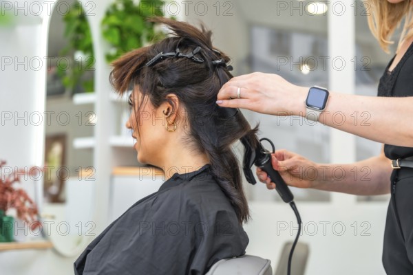 Hairdresser styling client's hair with curling iron in a modern beauty salon, creating a