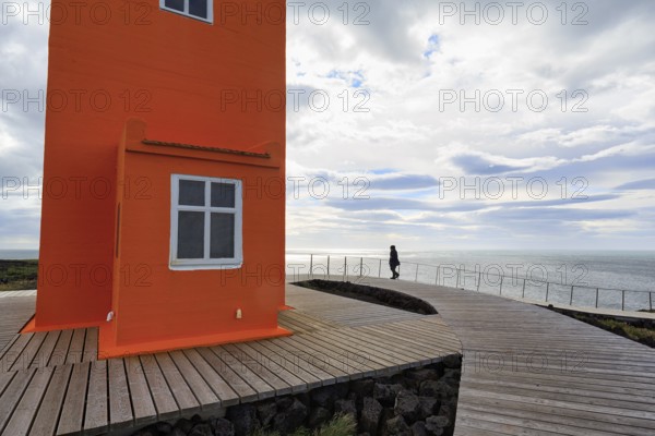 Orange lighthouse Skálasnagaviti or Svörtuloft with wooden plank path, walker, Skalasnagi,