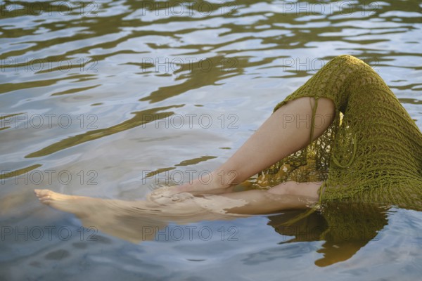 Warm sunlight casts a golden hue on the lake as bare legs dangle from a crochet skirt, creating