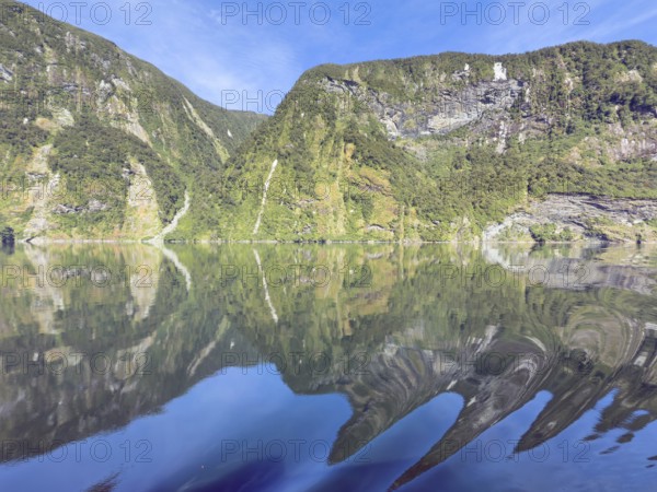 Mountains with reflections in the water against a blue sky in Doubtful Sound, South Island, New