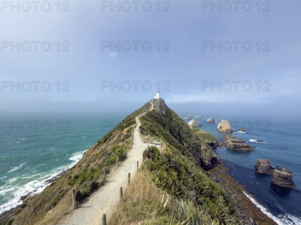 Nugget Point Lighthouse with Nugget Rocks in front of a blue sky, South Island, New Zealand,