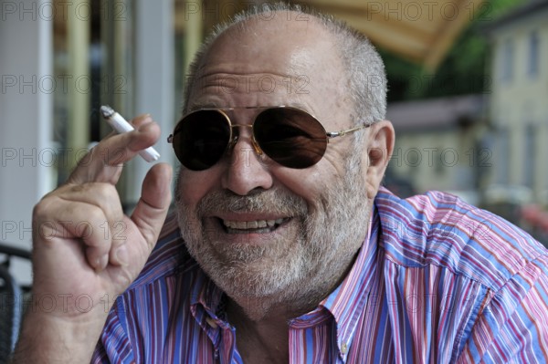 Portrait of a smiling elderly gentleman with a beard, sunglasses and a cigarette in his hand,