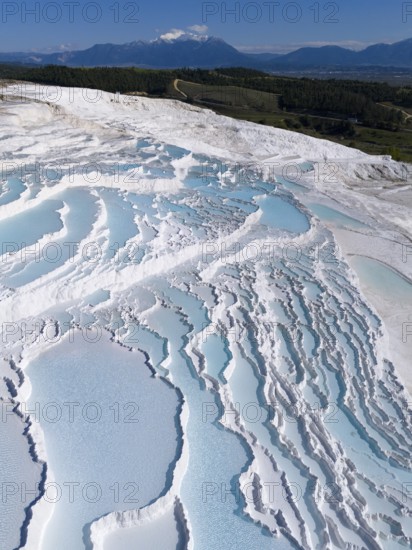 Cascading terraces of turquoise water and white limestone in the foreground, mountains in the