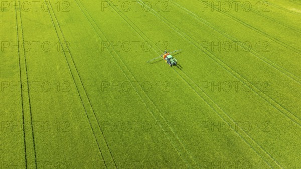 Farmer with tractor working in the field. In early summer, he fertilises the grain for an optimum