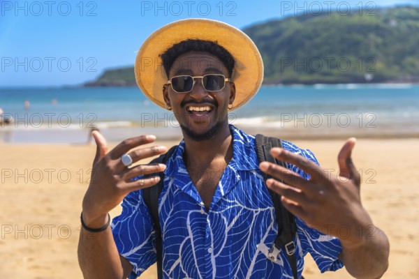 Young man wearing a hat and sunglasses, joyfully gesturing with his hands while enjoying the sunny