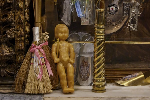 Symbolic objects in a religious context, including doll and broom, framed by gilded decorations,
