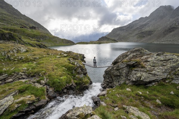 Mountaineer standing on a suspension bridge, mountain stream and mountain lake Wangenitzsee,