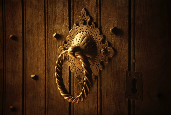 A beautifully designed door knocker sits prominently on a weathered wooden door. The warm lighting