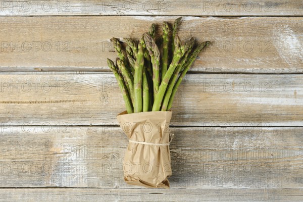 A bundle of fresh green asparagus is wrapped in brown paper and tied with twine, resting on a