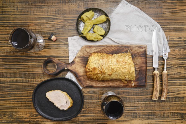 Overhead view of roasted pork meat and pickled peppers on a wooden table accompanied with red wine