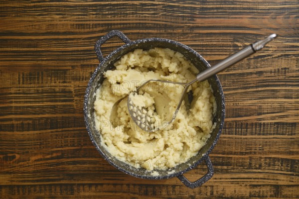 Creamy mashed potatoes are freshly prepared in a pot, sitting on a rustic wooden table. A potato