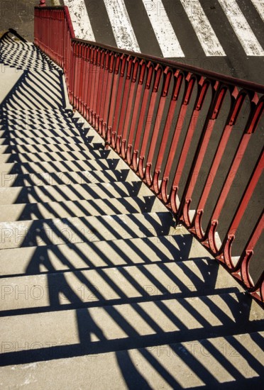 Bright sunlight creates intriguing patterns as shadows fall from red railings onto stone steps next