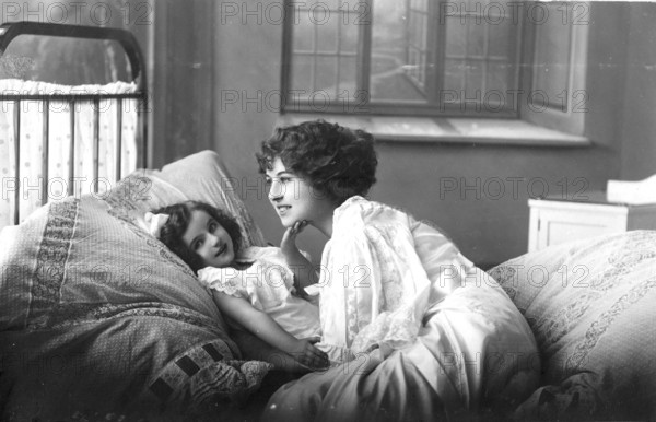 Woman with daughter, 1920s, A mother lies down with her child in bed, showing affection in a cosily