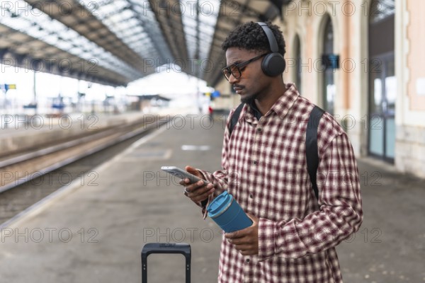 Stylish commuter using a mobile phone while enjoying music through headphones at a bustling train