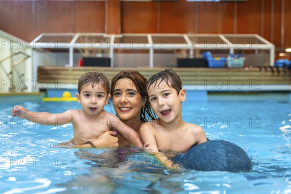 Mother and two sons smiling and playing in a swimming pool, enjoying a family moment of fun and