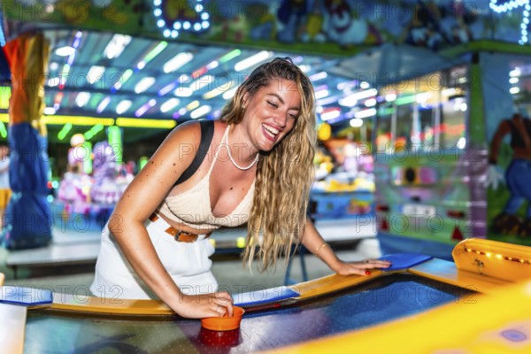 Young woman enjoying a game of air hockey at a brightly lit amusement park, laughing and having a