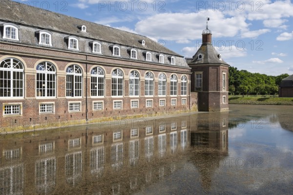 Historic brick building reflected in calm water under a blue sky and clouds, Nordkirchen Castle,