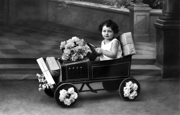 Child in toy car, 1920s, A child drives a toy car, decorated with flowers, in a nostalgic black and