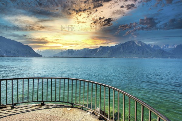 Golden light reflects on the calm waters of Lake Leman as clouds gather over the mountains in