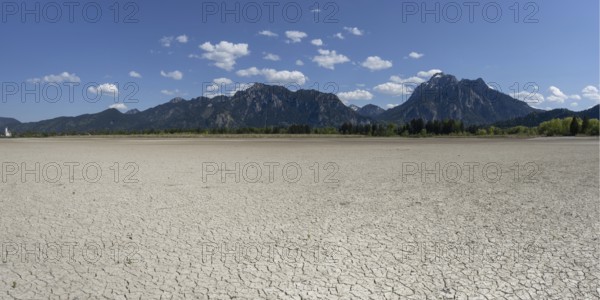 Cracked, dried out ground, waterless Forggensee in spring, behind it Tegelberg massif and Säuling,