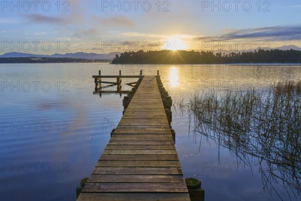 Wooden footbridge leading into the water at sunrise over a calm lake, Lake Mahinapua, Ruatapu,