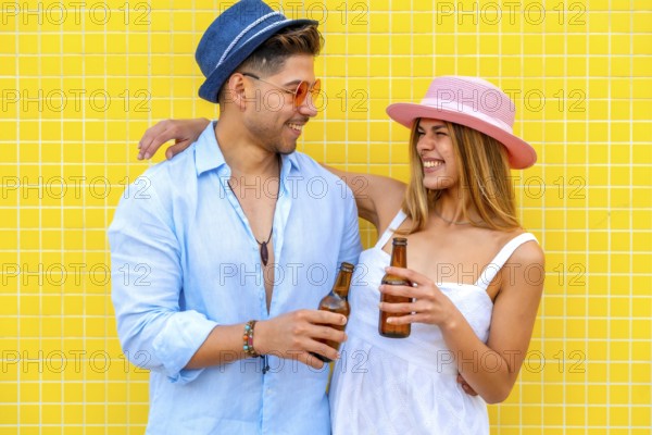 Young tourists drinking bottled beer, wearing summer clothes and hats, smiling and having fun on a