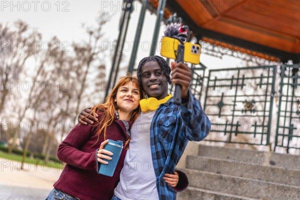 Two young content creators are recording a video blog in a park, using a smartphone attached to a
