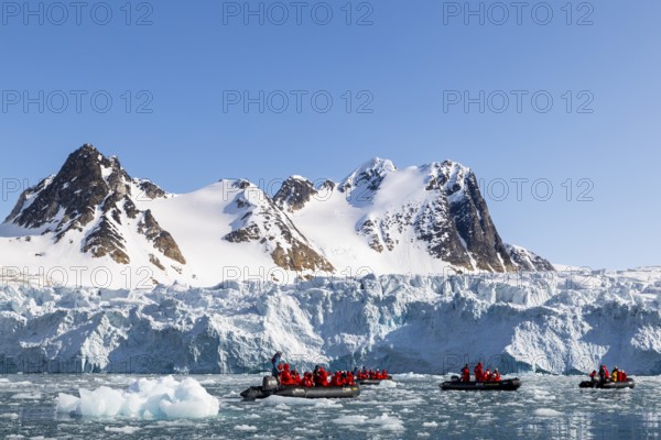 Group of Zodiacs in front of glacier and mountain range with snow, sea, Fugelfjorden, Spitsbergen,