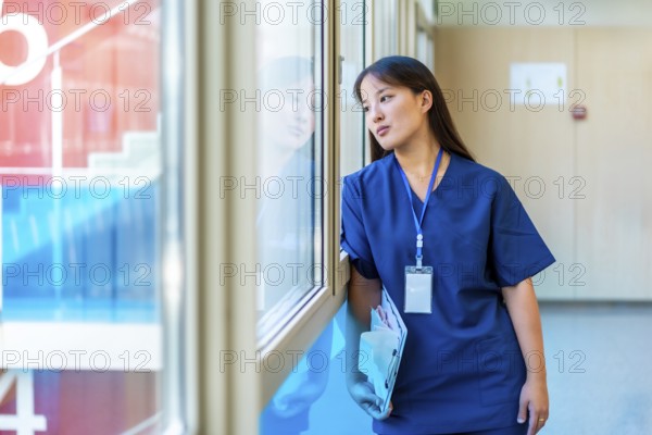 Thoughtful medical professional pausing in hospital hallway, holding patient files and gazing