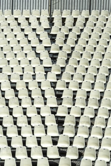 Rows of empty white seats fill a large stadium, creating a uniform pattern. The seating arrangement
