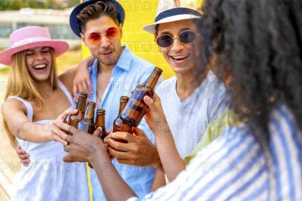 Cheerful multi ethnic friends enjoying a summer party, toasting with beer bottles against a vibrant
