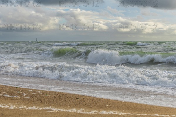 Powerful ocean waves wash over a sandy beach, creating white foam against a backdrop of dramatic