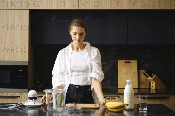 A woman stands in a contemporary kitchen, preparing to blend banana and sea buckthorn smoothies.