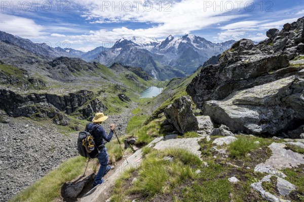 Mountaineer on hiking trail in mountain landscape, descent at Col du Louvie, view of mountain lake