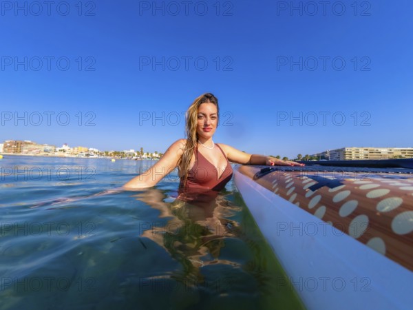 Woman wearing swimsuit relaxing in the sea next to her paddle board on a sunny summer day with a