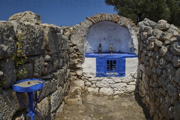 Stone chapel with blue window amidst ancient ruins, surrounded by natural walls and a deep blue