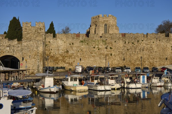 Boats moored in front of an old harbour wall with historic tower, Rhodes Old Town, Rhodes,