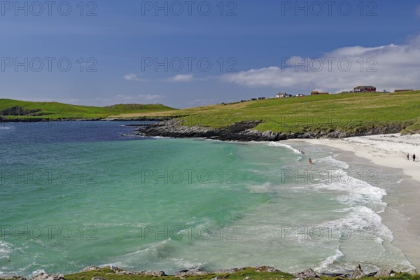 A picturesque beach with turquoise waters and gentle waves under a blue sky, surrounded by green