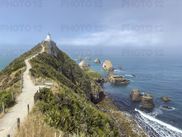 Nugget Point Lighthouse with Nugget Rocks in front of a blue sky, South Island, New Zealand,