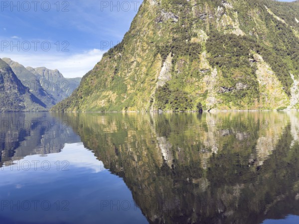 Mountains with reflections in the water against a blue sky in Doubtful Sound, South Island, New